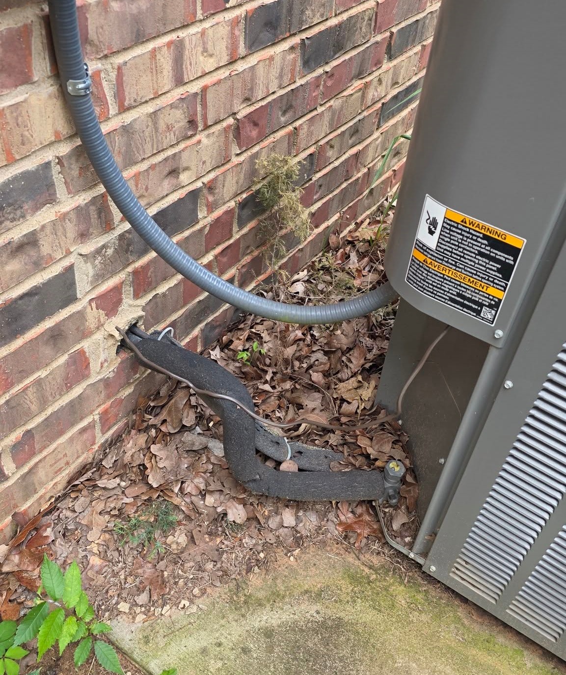 Deteriorated insulation on an HVAC refrigerant line beside the outdoor condenser