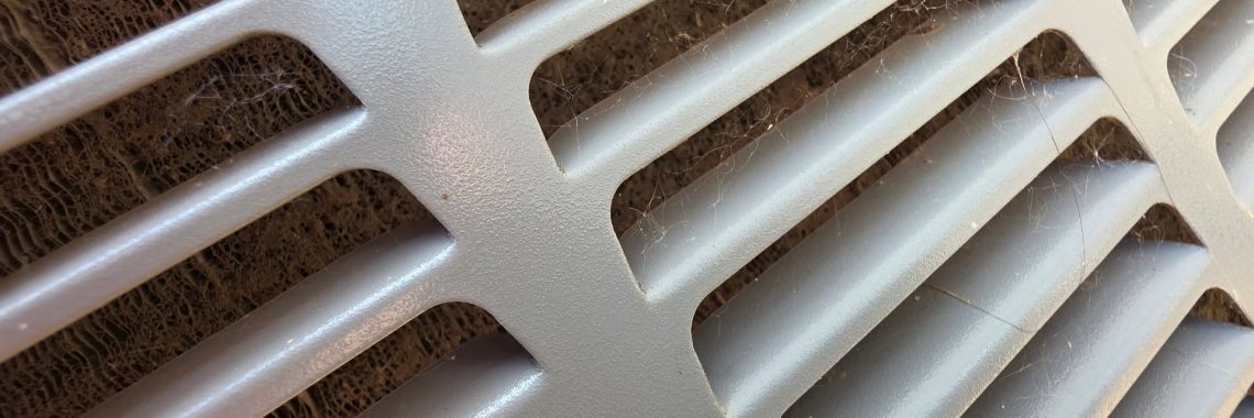 Outdoor HVAC condenser coil clogged with dirt, lint, and debris